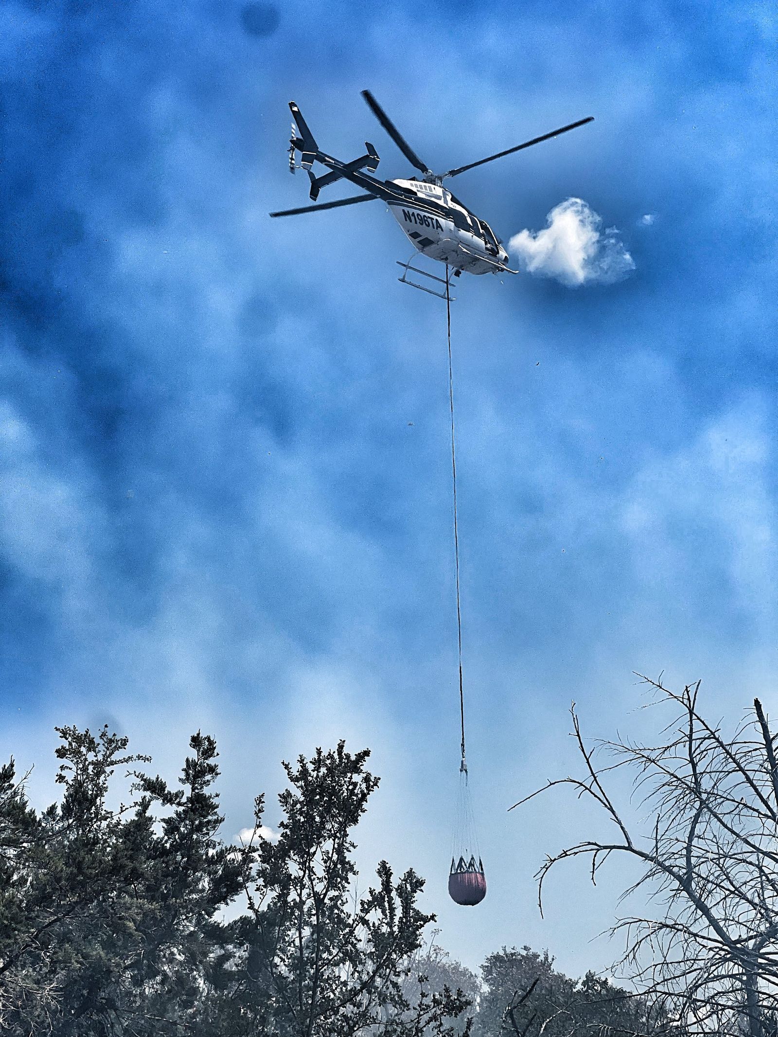 A helicopter drops water on a wildfire